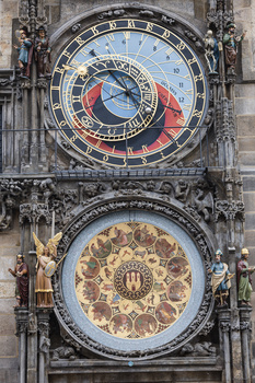 Ornate astronomical clock with two circular faces stacked vertically on a stone building facade.