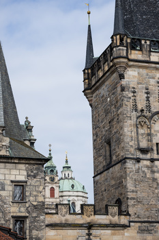 Historic stone towers with spires against a cloudy sky, featuring ornate architectural details and a domed structure in the background.