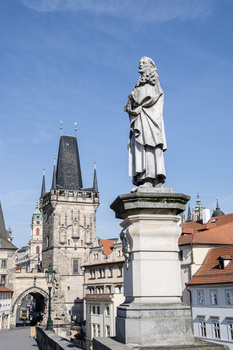 White stone statue on pedestal in European town square with Gothic tower in background.