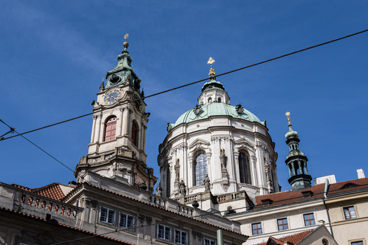 Two ornate church domes with golden crosses against a clear blue sky, framed by power lines.
