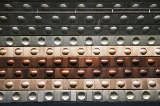 Geometric arrangement of hemispherical domes in rows across horizontal metal panels in varying neutral and warm tones.