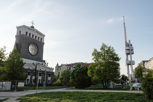Clock tower and communications tower anchoring a European public square with green lawn and surrounding buildings.
