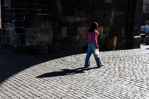 Child in purple shirt walking across cobblestone plaza with dark stone building backdrop.