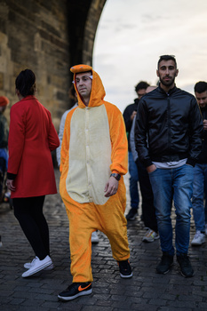 Person in orange and white onesie costume walking among other pedestrians on a stone street.