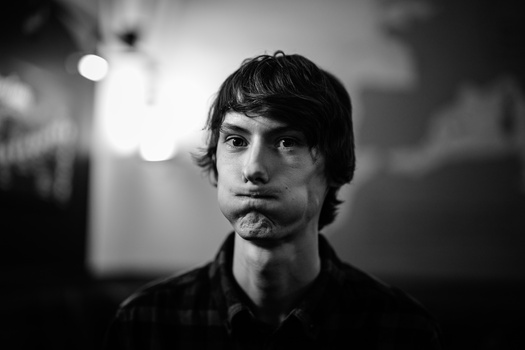 Black and white portrait of a man with shoulder-length dark hair and facial hair, looking directly at camera.