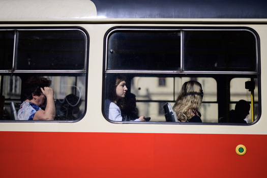 Passengers visible through windows of a red and white public transit bus, captured in natural daylight.