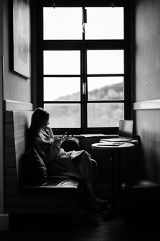 Person sitting by a multi-paned window reading at a desk in a high-contrast black and white photograph.
