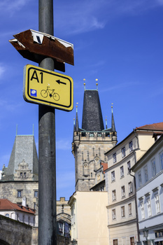 Street sign with worn arrow and yellow A1 route marker mounted on pole with Gothic tower in background.