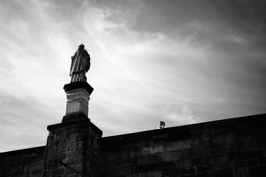 Statue atop a stone pedestal silhouetted against a dramatic cloudy sky.