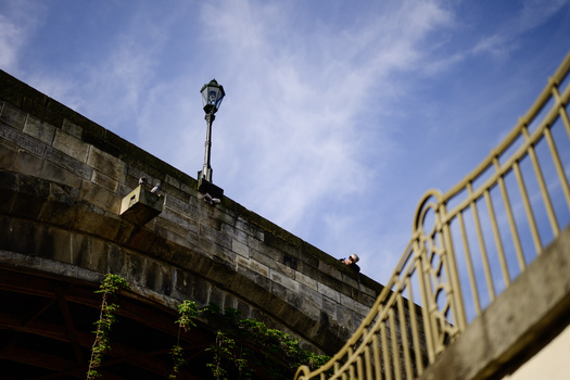 Stone bridge with ornate yellow metal railing and vintage lamp post against blue sky with clouds.