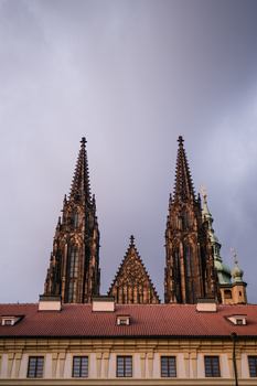 Gothic cathedral facade with twin spires against overcast sky and terracotta roofline below.