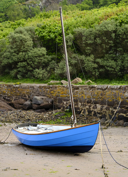 Blue sailboat resting on sand at low tide with moored rope and stone wall in background.
