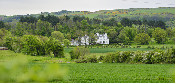 White Victorian mansion nestled among lush green trees in a rolling pastoral valley.