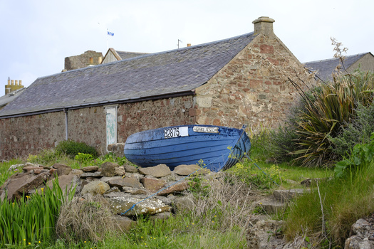 Blue fishing boat resting against stones beside a weathered stone cottage with slate roof.