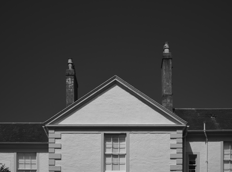 Black and white photograph of a symmetrical cottage with triangular gable and two chimneys.