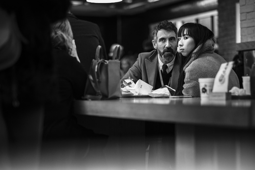 Man and woman sit at a table during what appears to be an interview or meeting, captured in black and white.