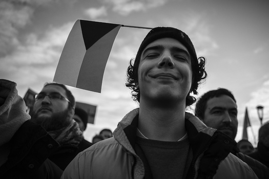 Man with curly hair looking upward among a crowd holding flags in black and white.