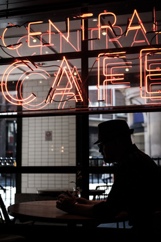 Silhouetted figure working at a laptop inside a storefront with glowing neon signage overhead.