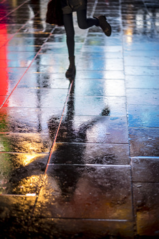 Runner's legs in motion on wet pavement with neon light reflections.