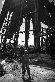 Person standing beneath towering industrial steel structure in black and white photograph.