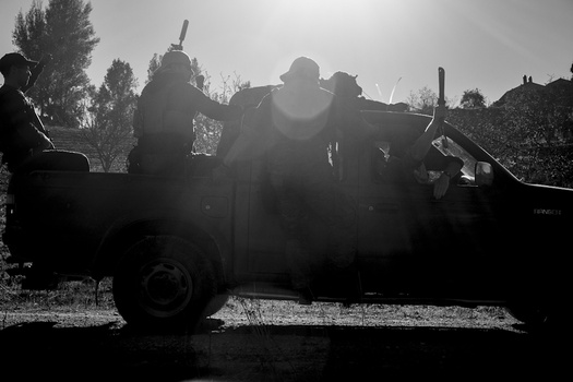 Silhouetted figures standing in the bed of an old military truck against a bright, overcast sky.