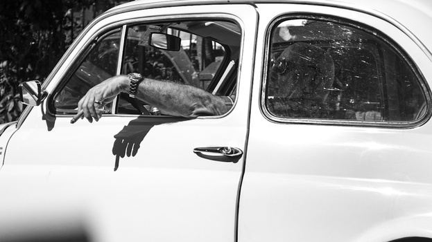 Man leaning out of a classic car window with arms extended downward in black and white.