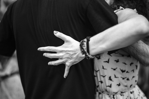 Bride and groom's hands together, showing wedding rings and beaded bracelets in black and white.