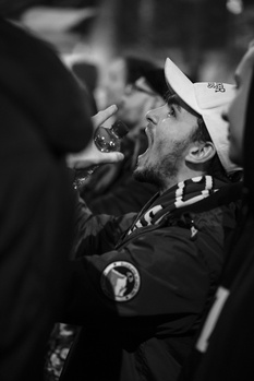 Man in cowboy hat and dark jacket smoking cigar, shot in black and white with dramatic lighting.
