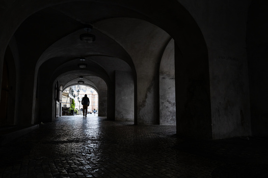 Dark arched stone passageway with figures silhouetted against bright daylight at the far end.
