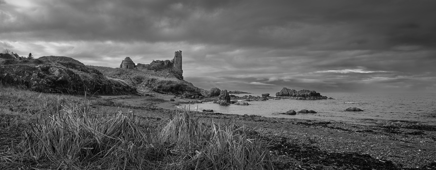 Rugged coastal landscape with rocky outcrops, grassy foreground, and dramatic overcast sky.