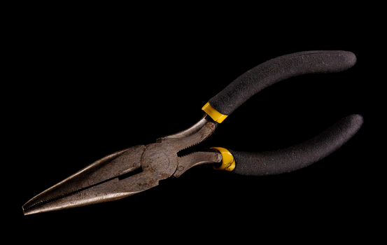 Vintage pliers with dark textured handles and brass ferrules against a black background.