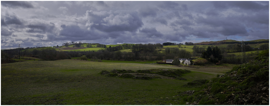 Rolling green hills with scattered trees, a distant farmhouse, and dramatic cloudy sky.