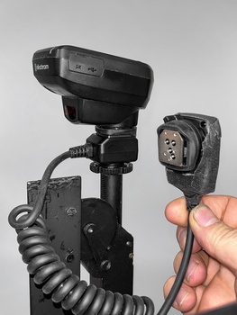Flash trigger receiver held in hand next to mounted camera flash and sync cable.