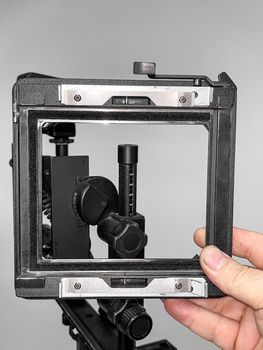Person holding a large format camera back showing internal bellows and ground glass focusing screen against gray background.
