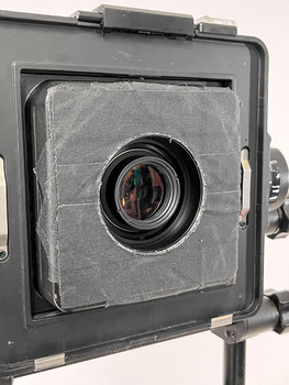 Large format camera with front lens element and ground glass back panel mounted on support stand.