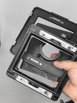 Hand holding an open camera body showing internal mirror mechanism and sensor assembly.