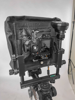 Professional cinema camera mounted on tripod with protective rain cover and external monitor attached.
