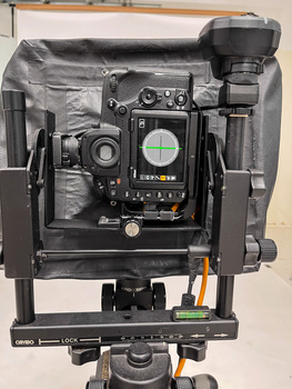 Large format cinema camera mounted on fluid head tripod, front view showing lens, matte box, and external monitor.