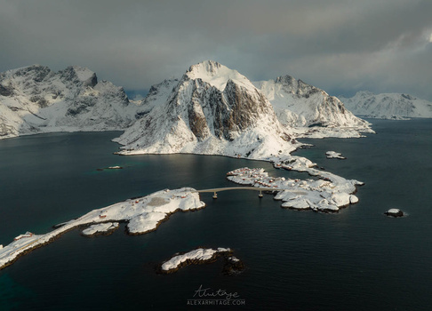 Snow-covered mountain peak surrounded by dark ocean water and smaller rocky islands.