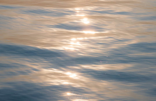 Sunlight reflecting off rippled water surface with golden and blue tones.