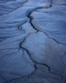 Aerial view of blue glacial ice with deep crevasses creating intricate curved patterns across the surface.