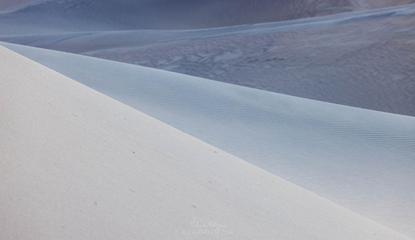 Layered sand dunes with rippled textures and soft shadows creating depth across white and gray tones.