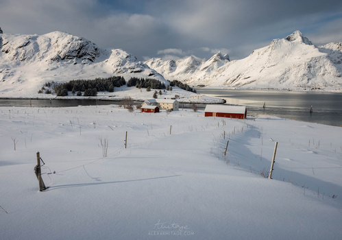 Snow-covered landscape with distant snow-capped mountains, frozen lake, and scattered buildings with red roofs.