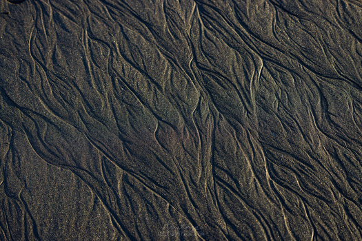 Close-up of wet sand surface with intricate ripple patterns and flowing water channels.