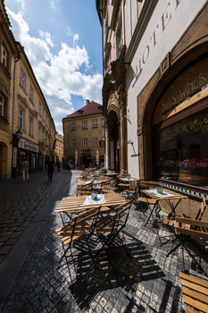 Outdoor café seating in a European cobblestone plaza with historic architecture and blue sky.