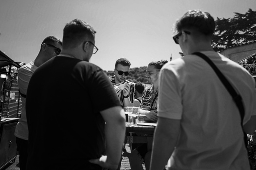 Five people gathered outdoors in black and white, viewing something on a table or surface in the center.