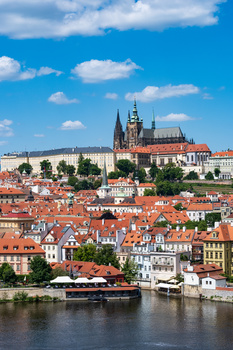 Prague cityscape with red-roofed buildings along the Vltava River and a Gothic cathedral on the hill.