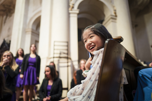 Young girl laughing while sitting in a wooden pew inside a classical building with white columns.
