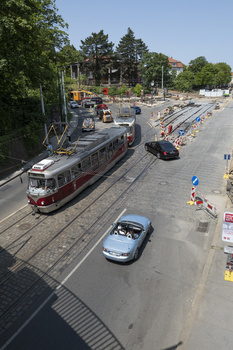 Elevated view of urban street with red tram, blue car, and pedestrians near construction site.