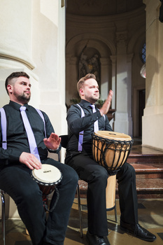 Two musicians sitting indoors playing hand drums during a performance.